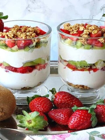 Two glass coffee cups filled with layered Greek Yogurt Parfait with kiwi and strawberries as garnish