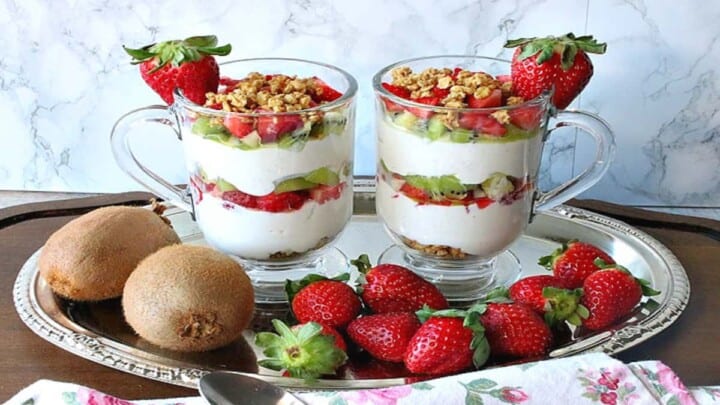 Two glass coffee cups filled with layered Greek Yogurt Parfait with kiwi and strawberries as garnish