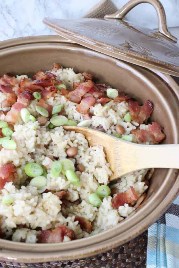 A vertical closeup photo of some Hoppin' John rice and beans casserole in a dish with a wooden spoon.