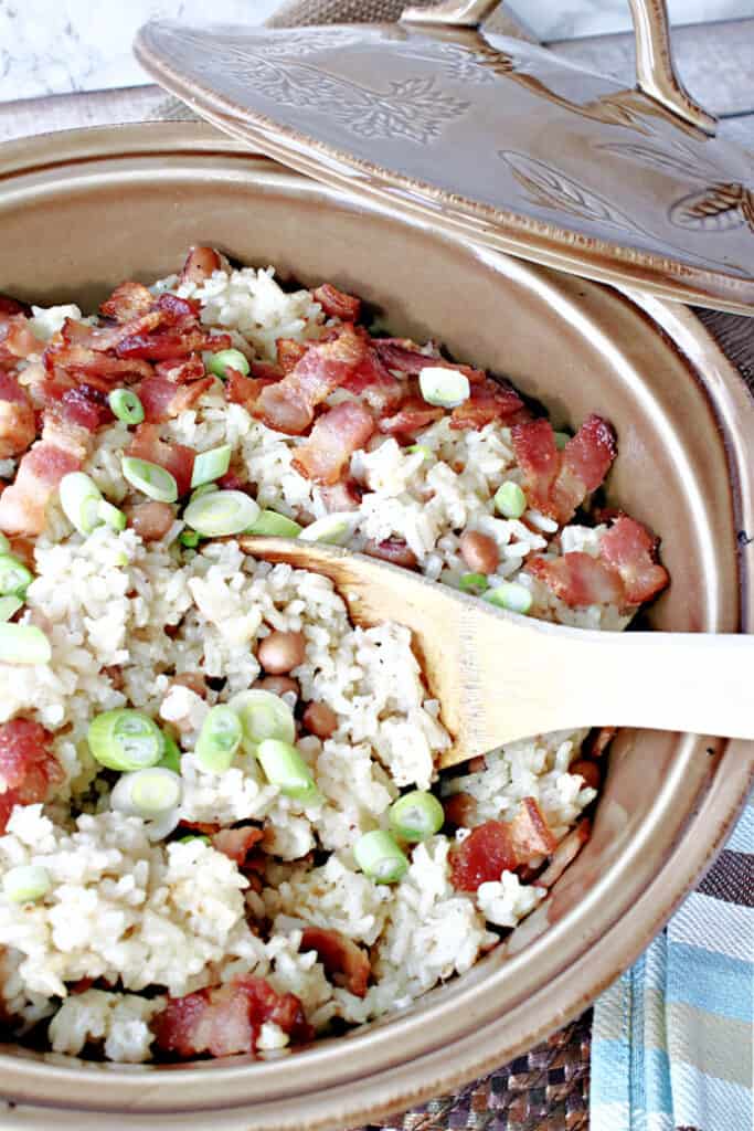 A vertical closeup photo of Hoppin' John with rice, beans, and scallions in a tan casserole dish.