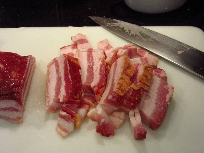 Slab bacon on a cutting board with a knife.