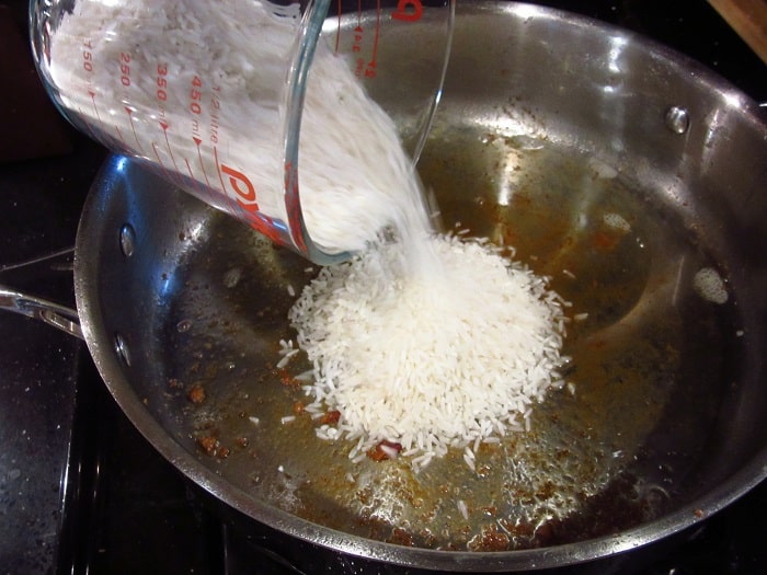 Rice being added to a skillet with bacon fat.