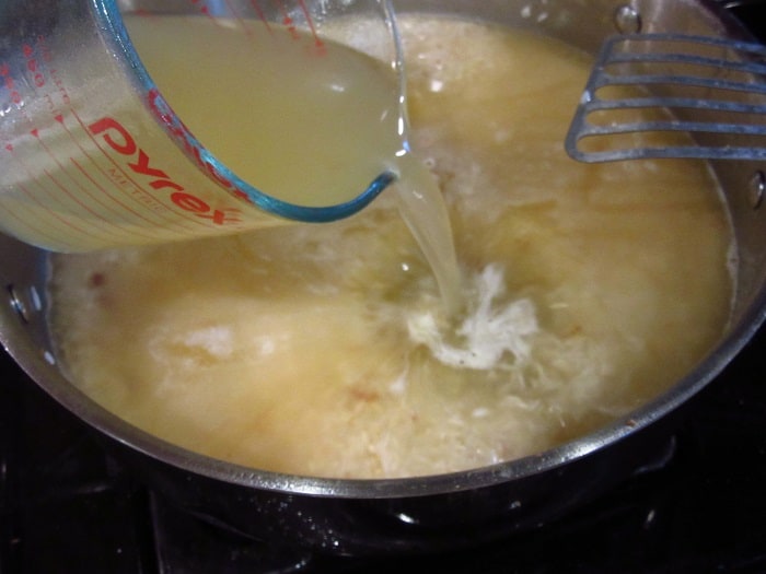 Chicken stock being added to a skillet with rice.