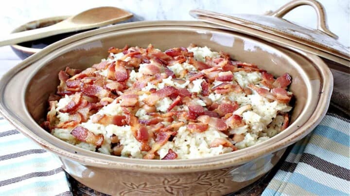 A tan casserole dish filled with Hoppin' John with a spoon and a casserole lid in the background.
