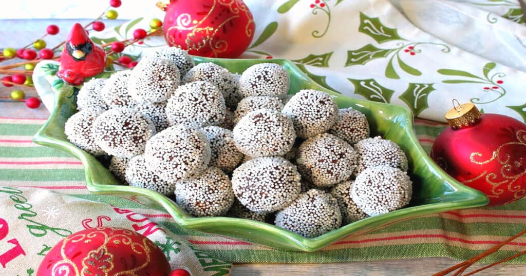 A cute holly berry bowl filled with Nonpareil Chocolate Peppermint Truffles with holiday napkins and ornaments on the side.