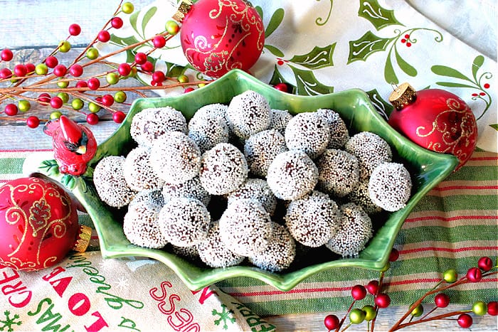 An overhead photo of a fun holly berry bowl filled with Nonpareil Chocolate Peppermint Truffles with ornaments and Christmas napkins in the background.