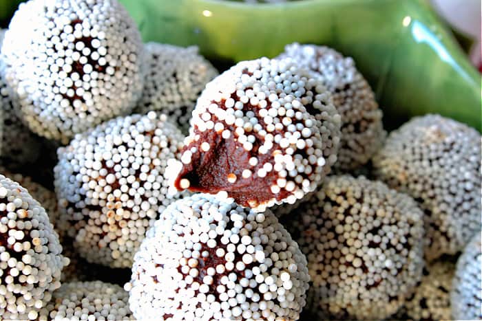 An extreme closeup photo of a chocolate peppermint truffle with white nonpareils and a bite taken out.