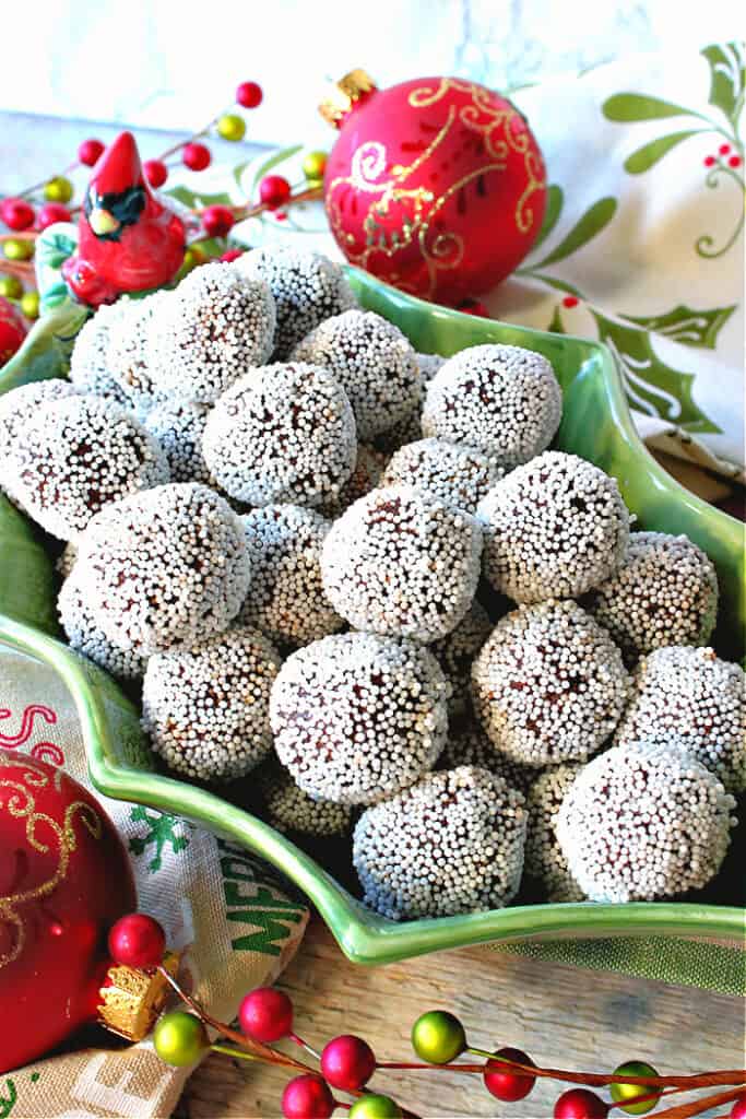 A vertical closeup of Nonpareil Chocolate Peppermint Truffles in a cute holly berry bowl with a red cardinal on the side.