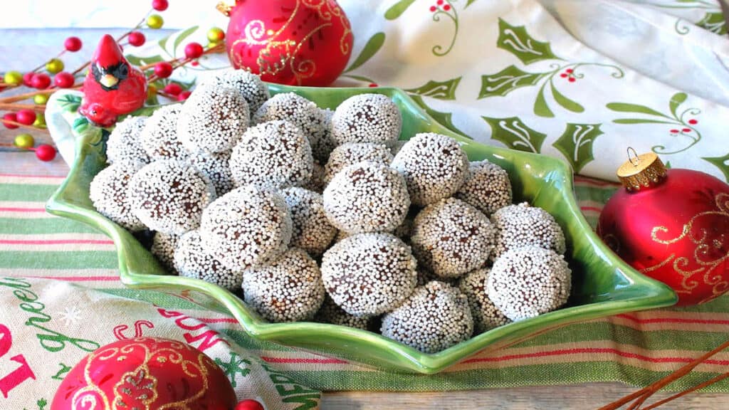 A cute holly berry bowl filled with Nonpareil Chocolate Peppermint Truffles with holiday napkins and ornaments on the side.