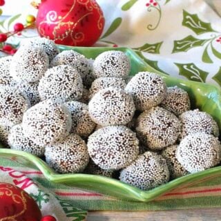 A cute holly berry bowl filled with Nonpareil Chocolate Peppermint Truffles with holiday napkins and ornaments on the side.