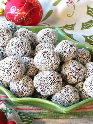 A cute holly berry bowl filled with Nonpareil Chocolate Peppermint Truffles with holiday napkins and ornaments on the side.