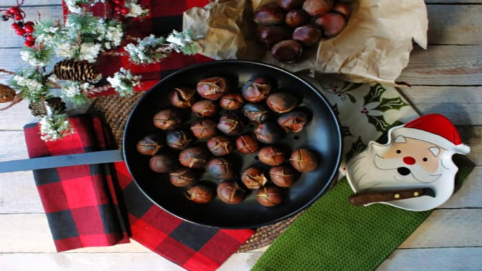 Direct overhead photo of Roasted Chestnuts in a chestnut pan along with a Santa dish, chestnut knife, and festive napkins.