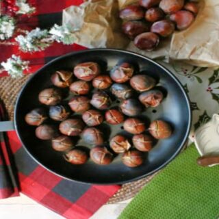 An overhead photo of a chestnut pan filled with Roasted Chestnuts along with some festive napkins and a chestnut knife.