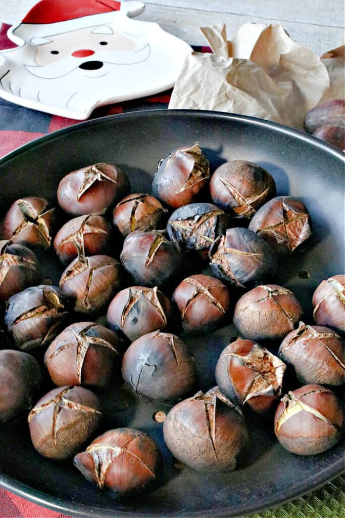 A vertical closeup image of Roasted Chestnuts in a chestnut pan along with a Santa dish in the background.