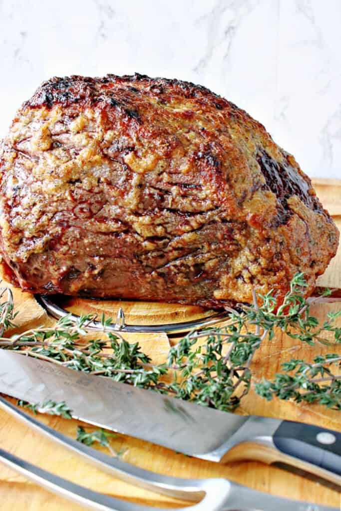 A Whoville Roast Beast on a wooden cutting board with a carving set and fresh herbs.