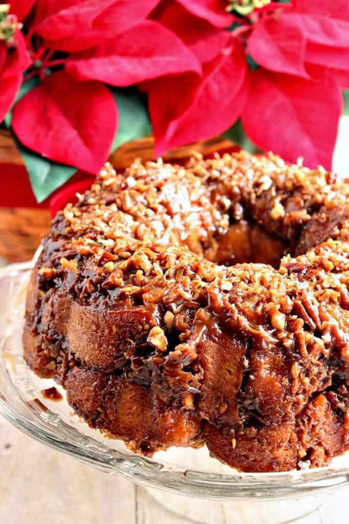 A vertical closeup image of a Coconut Caramel Crescent Ring with a vivid red poinsettia plant in the background.