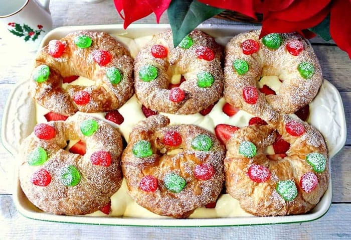 An overhead photo of a 13 x 9 casserole dish filled with Eggnog Pastry Cream Croissants along with strawberries, and red and green cherries on top.