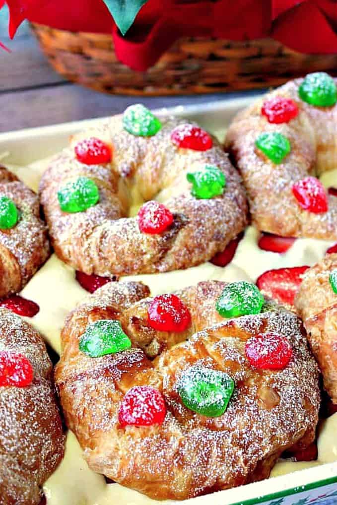 An extreme vertical closeup photo of Eggnog Pastry Cream Croissants with red and green glazed cherries and a confectioner's sugar dusting.