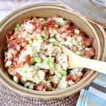 A round tan casserole dish filled with Hoppin John side dish with a wooden spoon.