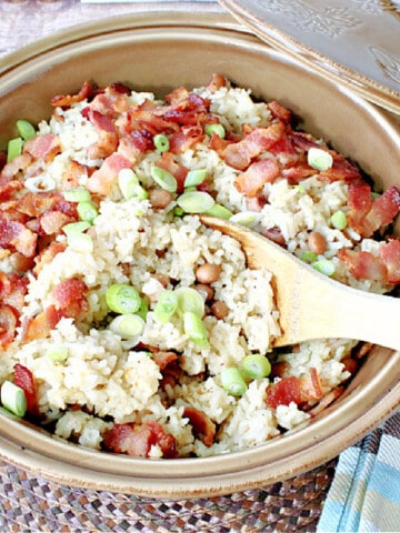 A round tan casserole dish filled with Hoppin John side dish with a wooden spoon.