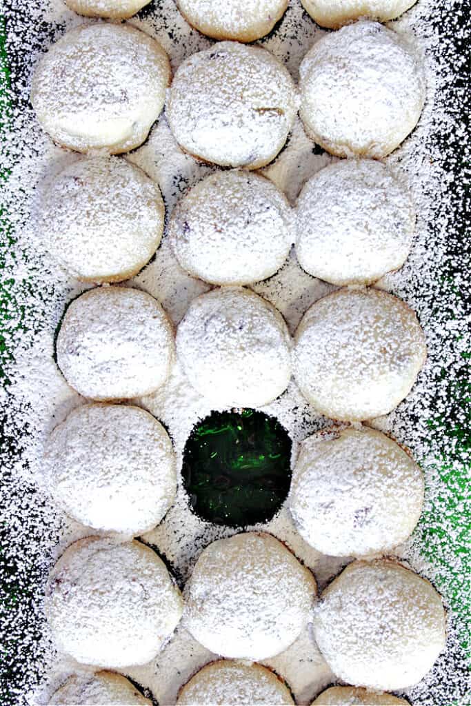 A vertical closeup of lined up snowballs cookies dusted with confectioners sugar with one missing 