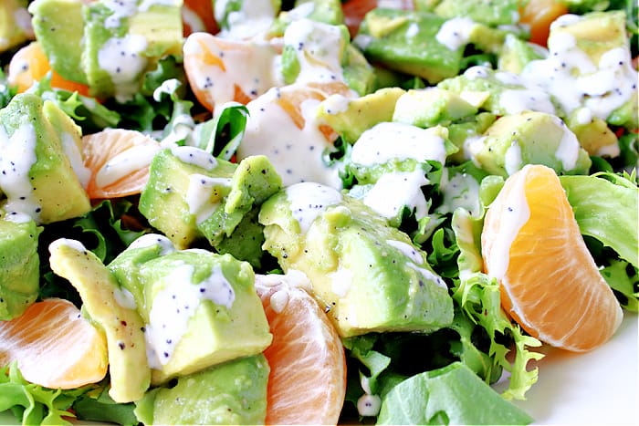 An extreme horizontal closeup photo of an Avocado Orange Salad drizzled with orange poppy seed dressing. 