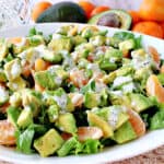 A horizontal photo of a green and orange Avocado Orange Salad in a large white bowl drizzled with poppy seed dressing.