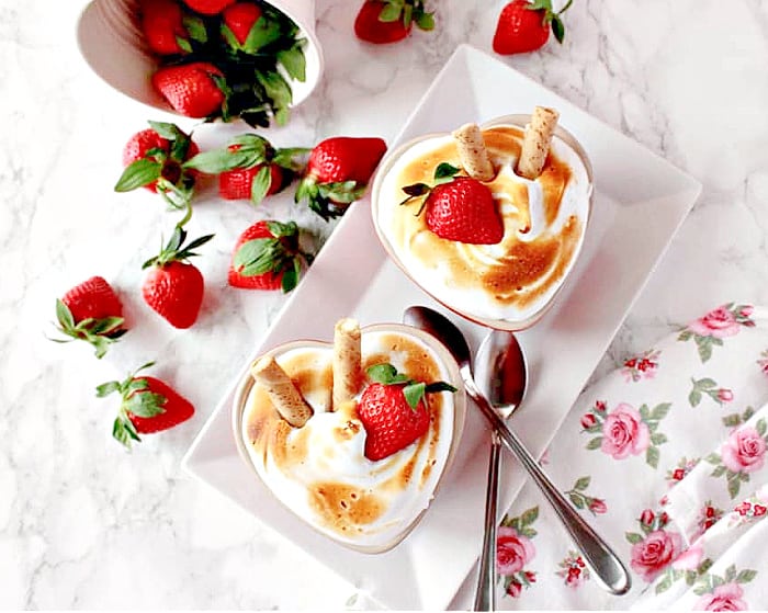 An overhead photo of two Baked Alaska for Two on a white plate with fresh strawberries as garnish and two ice cream spoons.