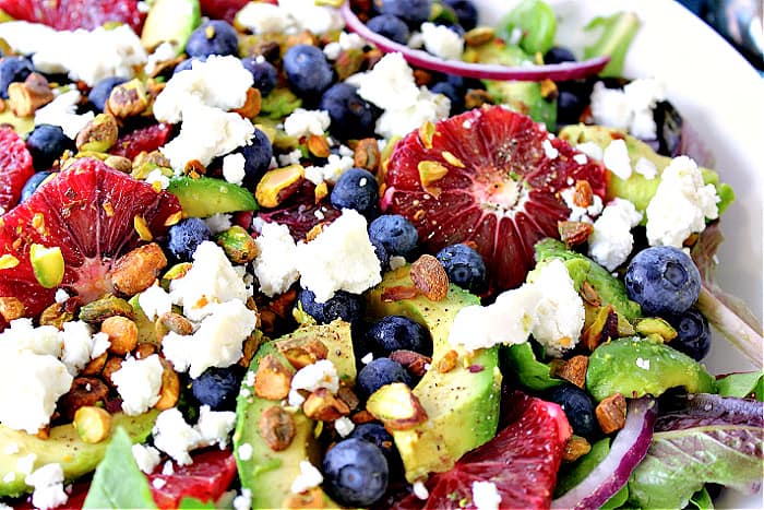 Super closeup photo of a Blood Orange Salad with avocado, feta cheese, pistachios, and blueberries.