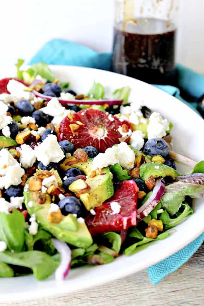 A closeup vertical Image of Blood Orange Salad with Blueberries and Feta along with pistachio nuts, red onion, and avocado.