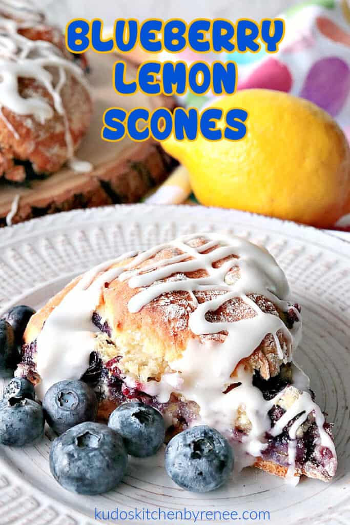 A vertical closeup image of a single Blueberry Lemon Scone on a white plate with fresh blueberries and a lemon in the background.