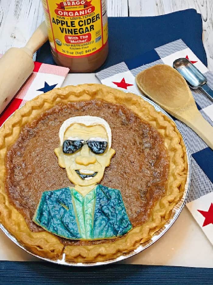 A vertical overhead photo of Joe Biden Vinegar Pie (PIE-den) with red, white, and blue napkins and a bottle of apple cider vinegar in the background.
