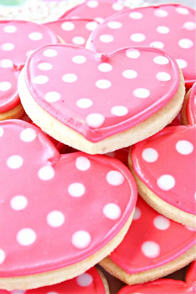 A closeup vertical side view of a plate of Polka Dot Heart Sugar Cookies with pink icing and white polka dots.