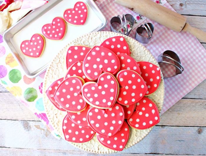 A direct overhead photo of a cake stand filled with pink and white Polka Dot Heart Cookies with a pink and white napkin and a multi colored polka dot napkin in the background.