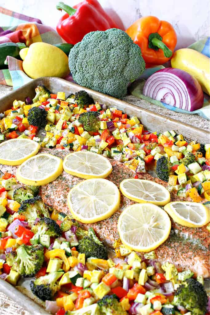 A colorful vertical photo of a sheet pan Rainbow Trout on a sheet pan surrounded by colorful roasted vegetables.