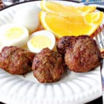Air Fryer Turkey Breakfast Sausages on a white plate along with a hard boiled egg and orange slices.