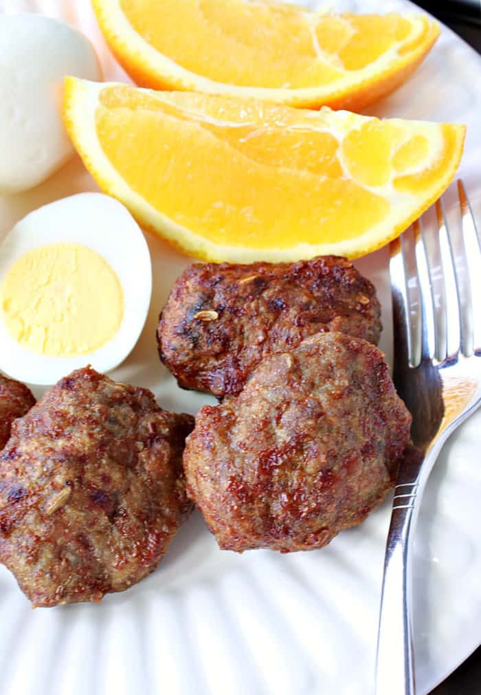 Vertical closeup image of air fryer Turkey Breakfast Sausage on a white plate with a hard boiled egg and some orange slices.