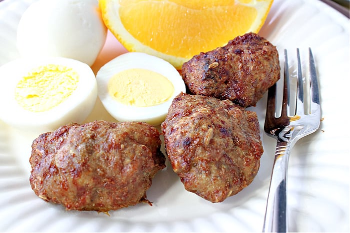 An overhead closeup photo of Turkey Breakfast Sausage on a plate with hard cooked eggs, a fork, and orange slices.