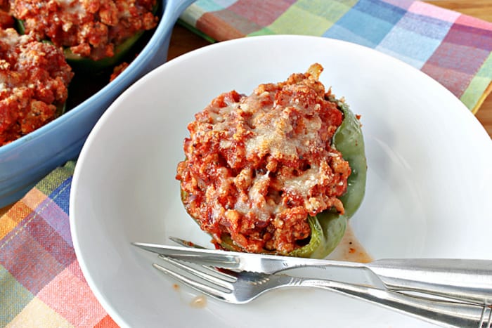 A Turkey Parmesan Stuffed Pepper half in a white bowl with a fork and a knife.