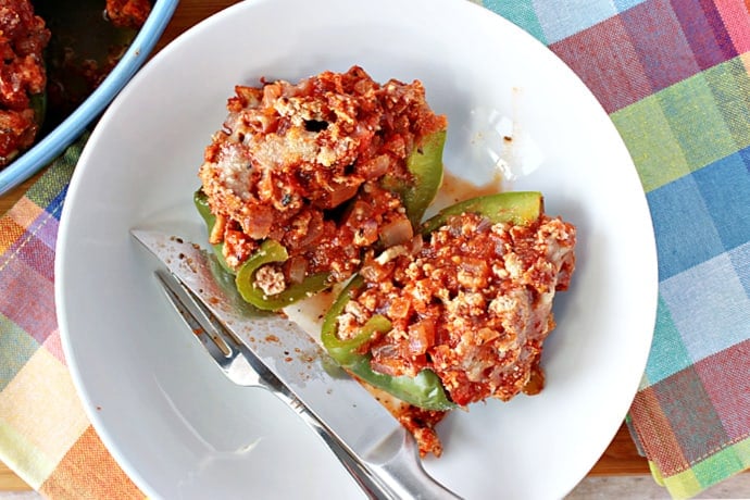 A direct overhead photo of two Turkey Parmesan Stuffed Peppers in a white bowl with a fork and a knife.