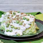 A horizontal photo of a Wedge Salad with Wasabi Peas on a brown and green plate with wasabi peas and grape tomatoes as garnish.