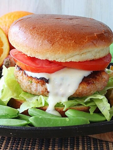 A Salmon Burger on a bun with sugar snap peas on the plate.