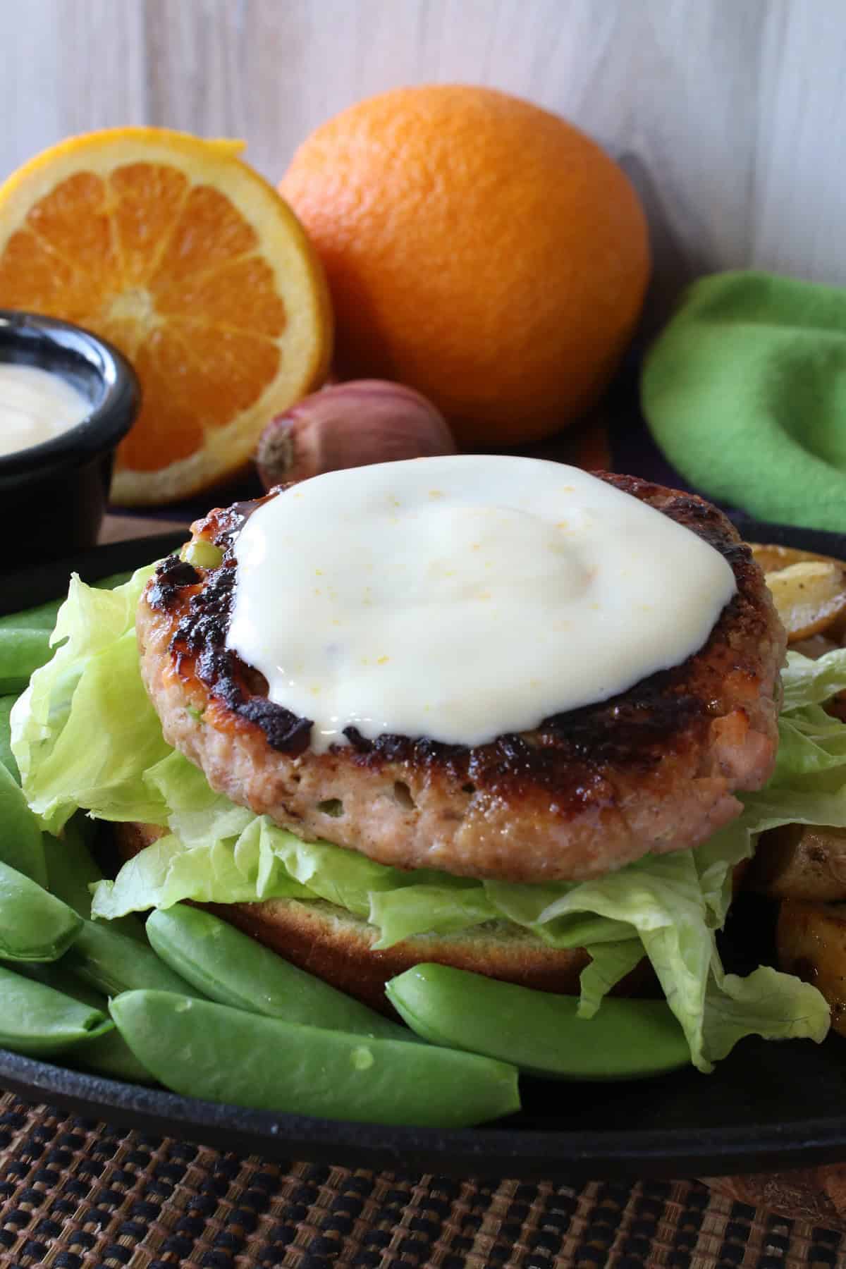 Salmon Burger with Miso and Sugar Snap Peas without a top bun and with orange sauce on the burger.