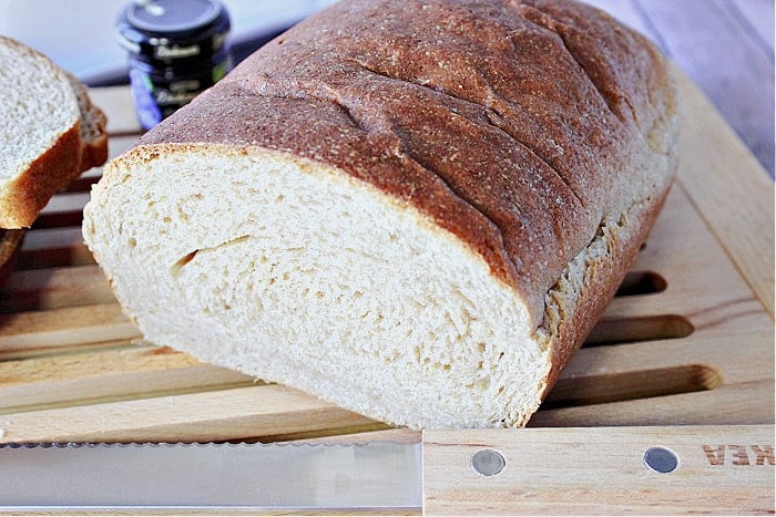 A loaf of Whole Wheat Honey Ricotta Bread that's been cut in half with a serrated knife in the foreground. 