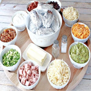 A large round wooden board loaded with the fixins for a Baked Potato Party Board.