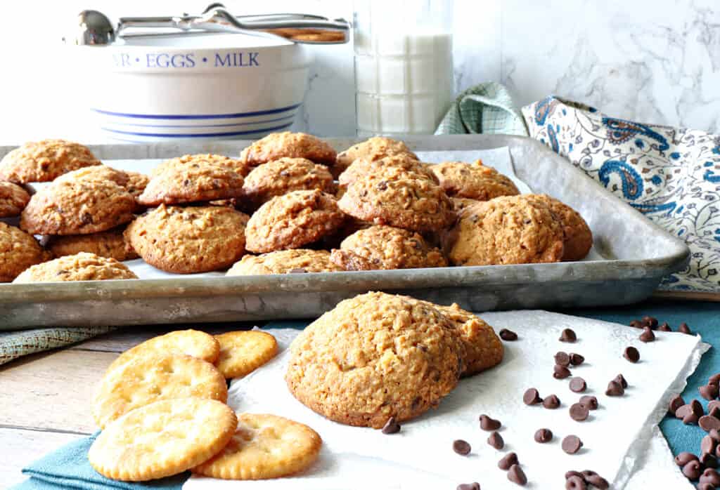 A horizontal photo of a full baking sheet with Butterscotch Ritz Cookies in the background and a few cookies with crackers and chocolate chips in the foreground.