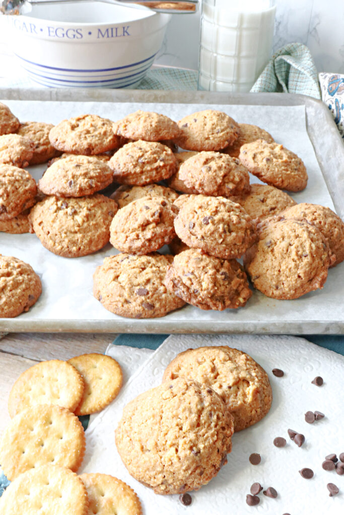 A vertical photo of a baking sheet filled with Butterscotch Ritz Cookies along with a few crackers and some chocolate chips in the foreground.