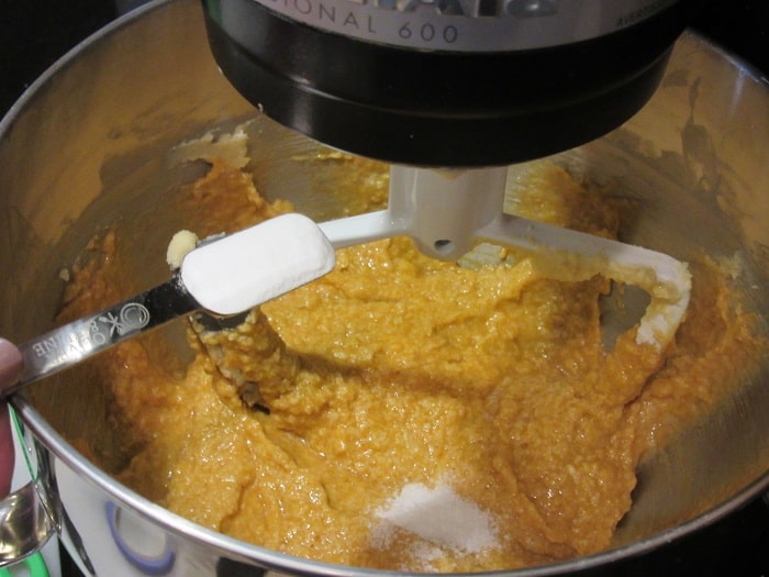 Salt being added to a stand mixer with cookie dough.
