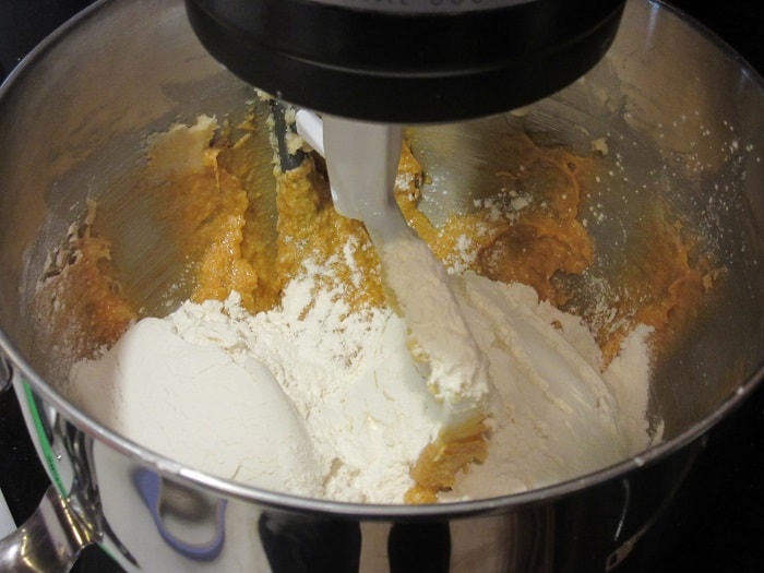Flour being added to a stand mixer with cookie dough.