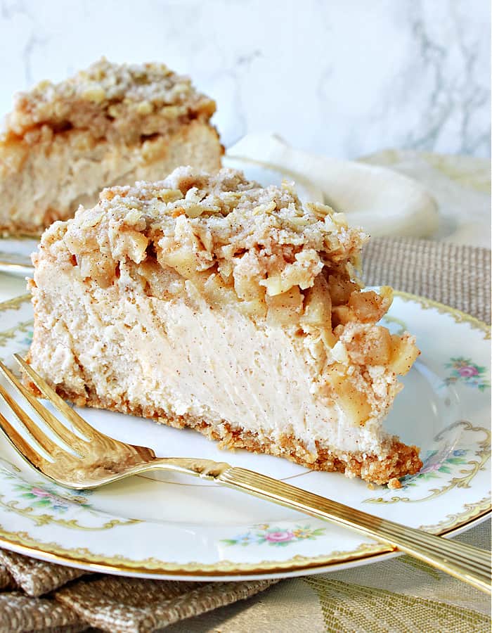 A creamy slice of Dutch Apple Cheesecake on a china plate with a gold fork in the forefront. 